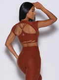 Back profile view of a model facing to her right wearing  our open back tee in Cinnamon color and a matching leggings