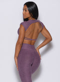 Back profile view of a model facing to her left wearing our open back tee in Regal Purple color and a matching leggings