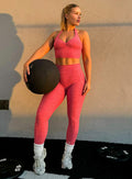 front profile view of a model holding a gym ball wearing our backless bra in Neon Tangerine Shock color along with the matching leggings