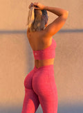 back profile view of a model adjusting her hair wearing our backless bra in Neon Tangerine Shock color along with the matching leggings