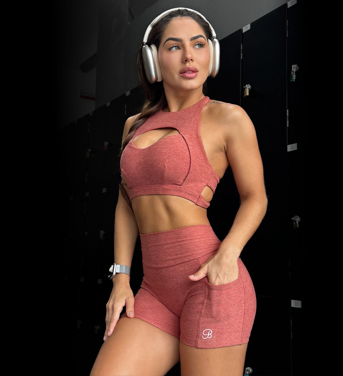 Front view image of model wearing women's active sports bra and matching v back shorts in pink while wearing headphones 