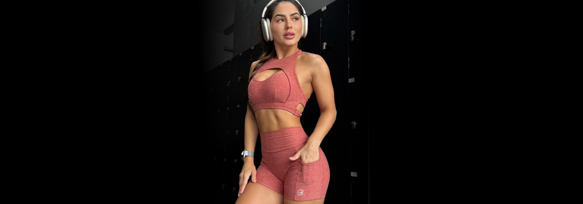 Front view image of model wearing women's active sports bra and matching v back shorts in pink while wearing headphones 