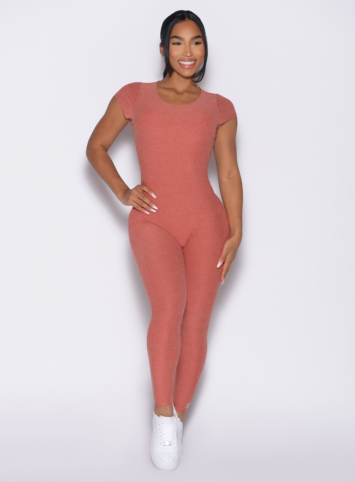 front profile view of a model with one hand on her waist wearing the Open Back Tee Bodysuit in Georgia Peach color