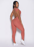 right side profile view of a model looking over her shoulder wearing the Open Back Tee Bodysuit in Georgia Peach color