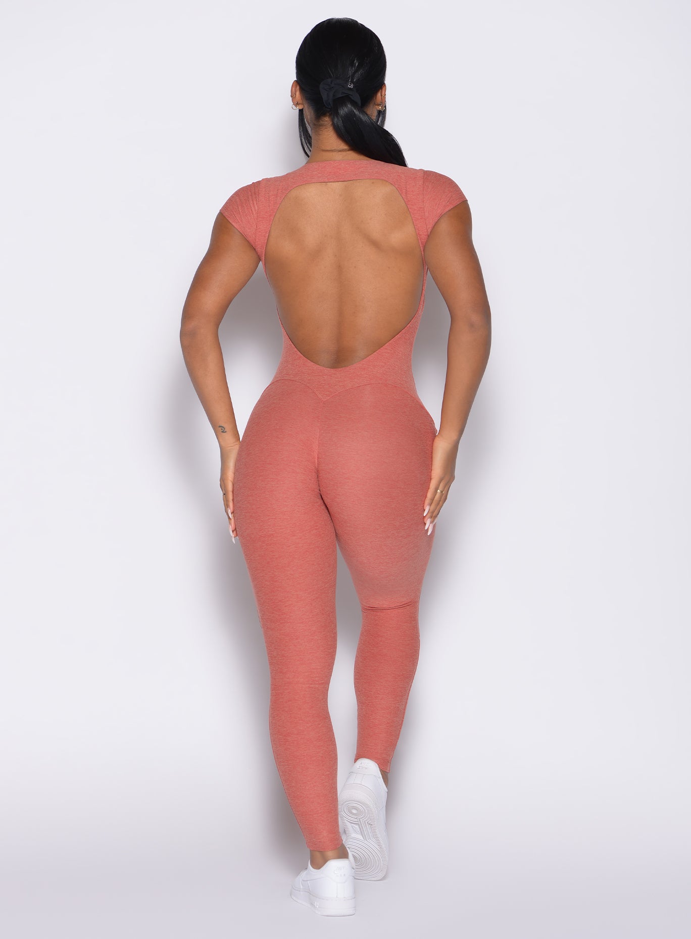 back profile view of a model with both hands on her thighs wearing the Open Back Tee Bodysuit in Georgia Peach color