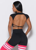 back  profile view of a model facing to her left  wearing our black open back tee along with a matching thigh high leggings