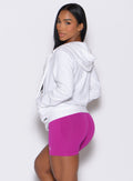 Left side profile view of a model facing to her left wearing our white oversized hoodie, along with shorts in berry color