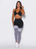 Front profile view of a model  facing forward wearing the Perform Thigh Highs in Black and Smoke color with three white stripes on the thighs and a black sports bra