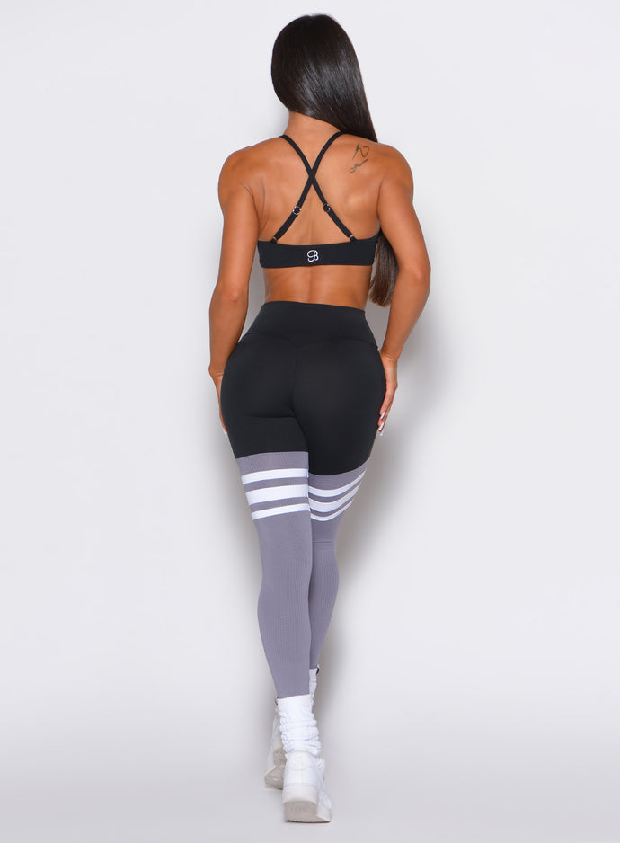 Back profile shot of a model wearing the Perform Thigh Highs in Black and Smoke color with three white stripes on the thighs and a black sports bra