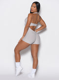 left side profile view of a model wearing our Backless Pocket Bodysuit Short in ice color