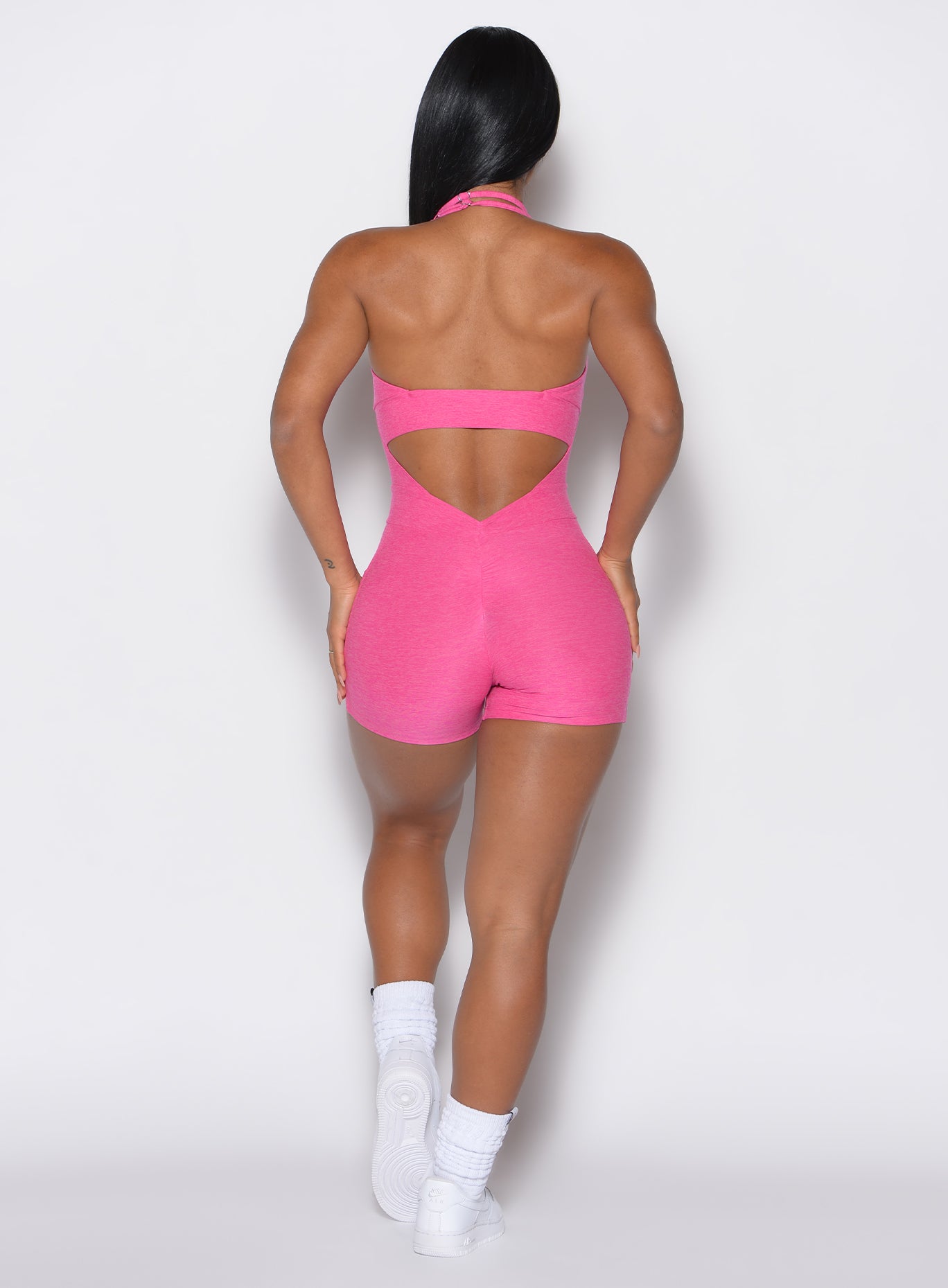 back profile view of a model wearing our Backless Pocket Bodysuit Short in pink glo color