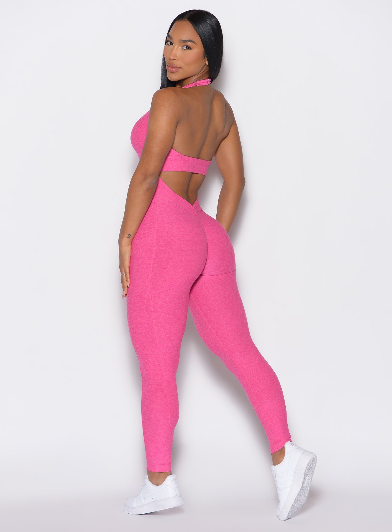 left side profile view of a model wearing our Backless Pocket Bodysuit in pink glo color