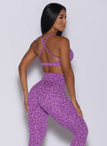 Back profile view of a model angled slightly to her right wearing our pumped sports bra in purple cheetah color and matching leggings