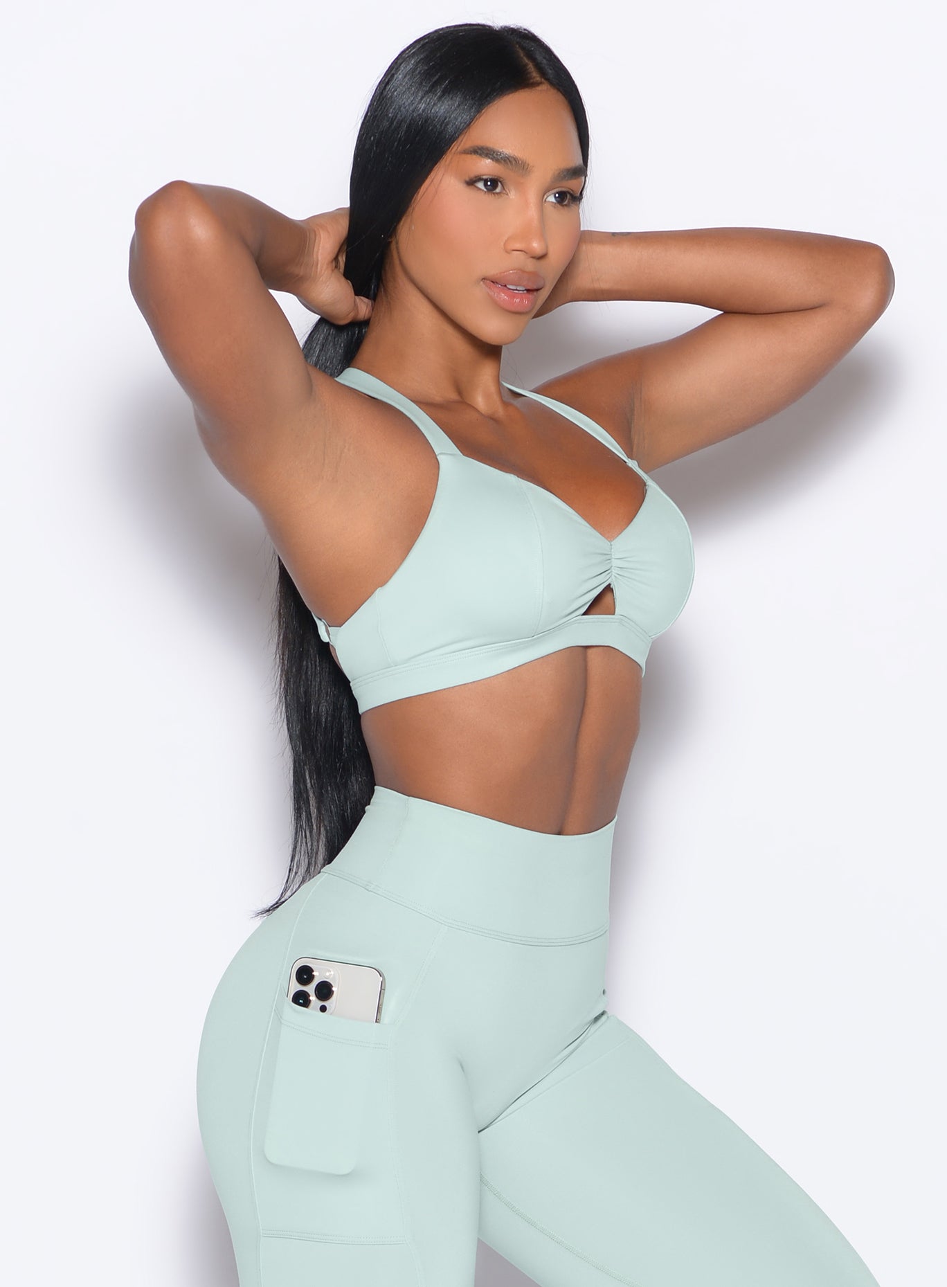 Front right side profile view of our model wearing the Sweetheart Sports Bra in Mist color in a hair tying pose. 