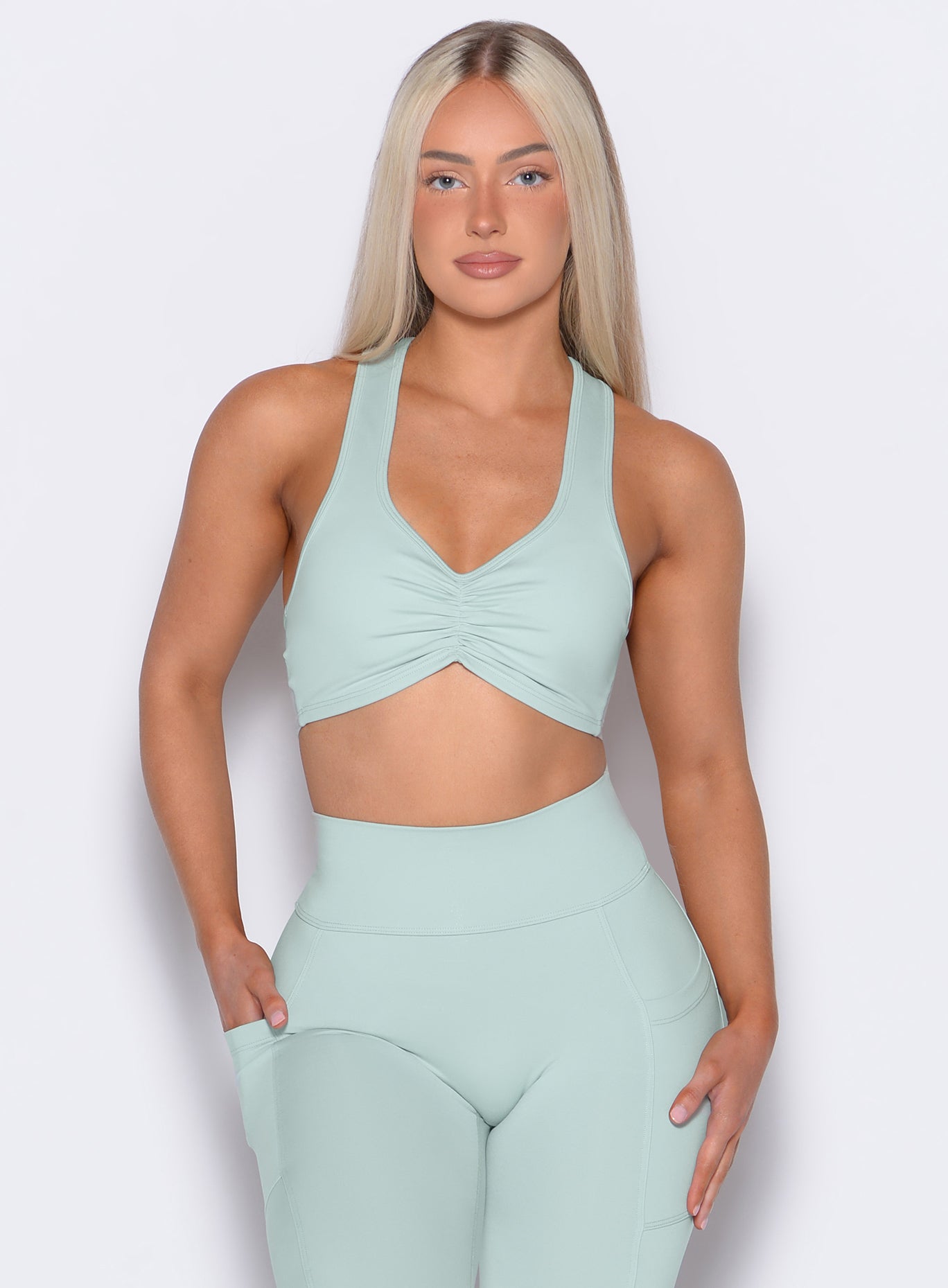 Front profile shot of our model with one hand inside the pocket of the leggings wearing the Scrunch Tank Bra in Mist color