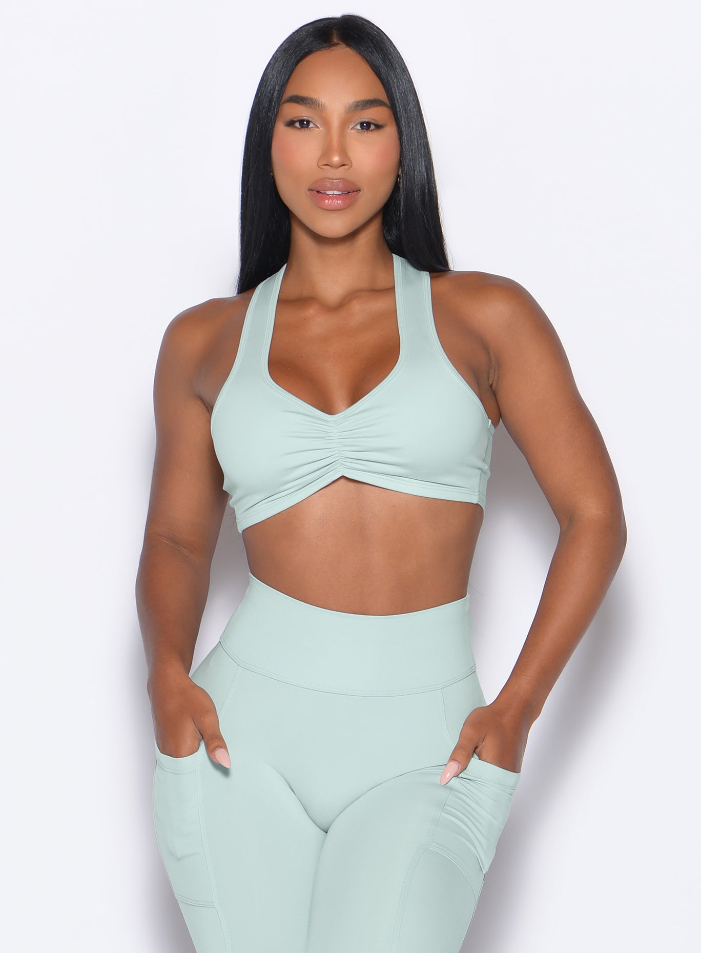 Front profile shot of our model with both hands inside the pockets of the leggings wearing the Scrunch Tank Bra in Mist color paired with the matching leggings