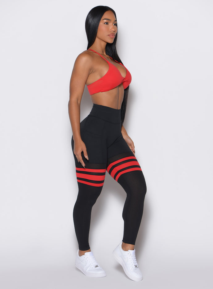 Right side profile view of a model facing forward wearing the Scrunch Thigh Highs in Black Fire color along with a red sports bra 