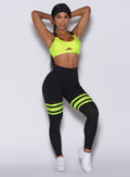 Front profile view of a model wearing our scrunch thigh high in black with neon yellow stripes on the thighs and a matching sports bra