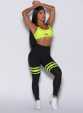 Front profile view of a model with her hands over her head wearing  our scrunch thigh high in black with neon yellow stripes on the thighs and a matching sports bra