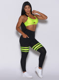 Right side profile view of a model looking at the floor wearing our scrunch thigh high in black with neon yellow stripes on the thighs and a matching sports bra