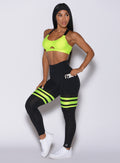 Left side profile view of a model angled to her left wearing our scrunch thigh high in black with neon yellow stripes on the thighs and a matching sports bra