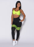 Front profile view of a model in our scrunch thigh high in black with neon yellow stripes on the thighs and a matching glow sports bra