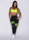 Front profile view of a model in our scrunch thigh high in black with neon yellow stripes on the thighs and a matching sports bra 