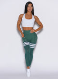 A front-profile picture of a model facing forward, showcasing our scrunch thigh-highs in emerald green embellished with three white stripes on the thighs. The ensemble is elegantly complemented by a matching white bra.