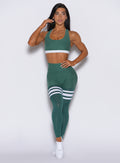 A front-profile picture of a model facing forward, showcasing our scrunch thigh-highs in emerald green embellished with three white stripes on the thighs. The ensemble is elegantly complemented by a matching tank bra.