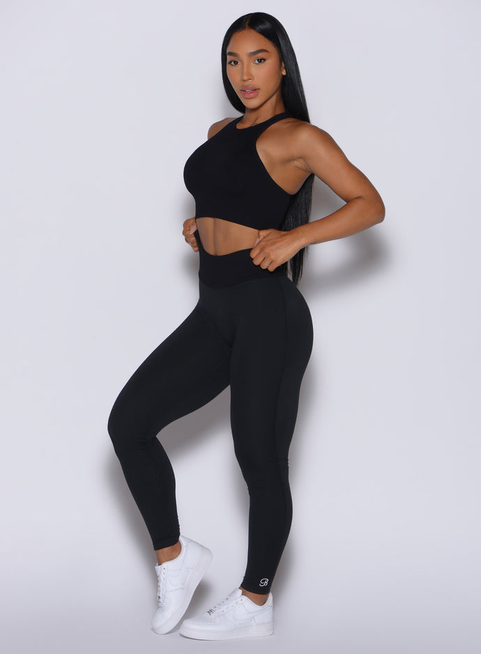 Front left side profile view of our model with both her hands on the waist of the leggings wearing the Figure Scrunch Leggings in Black color