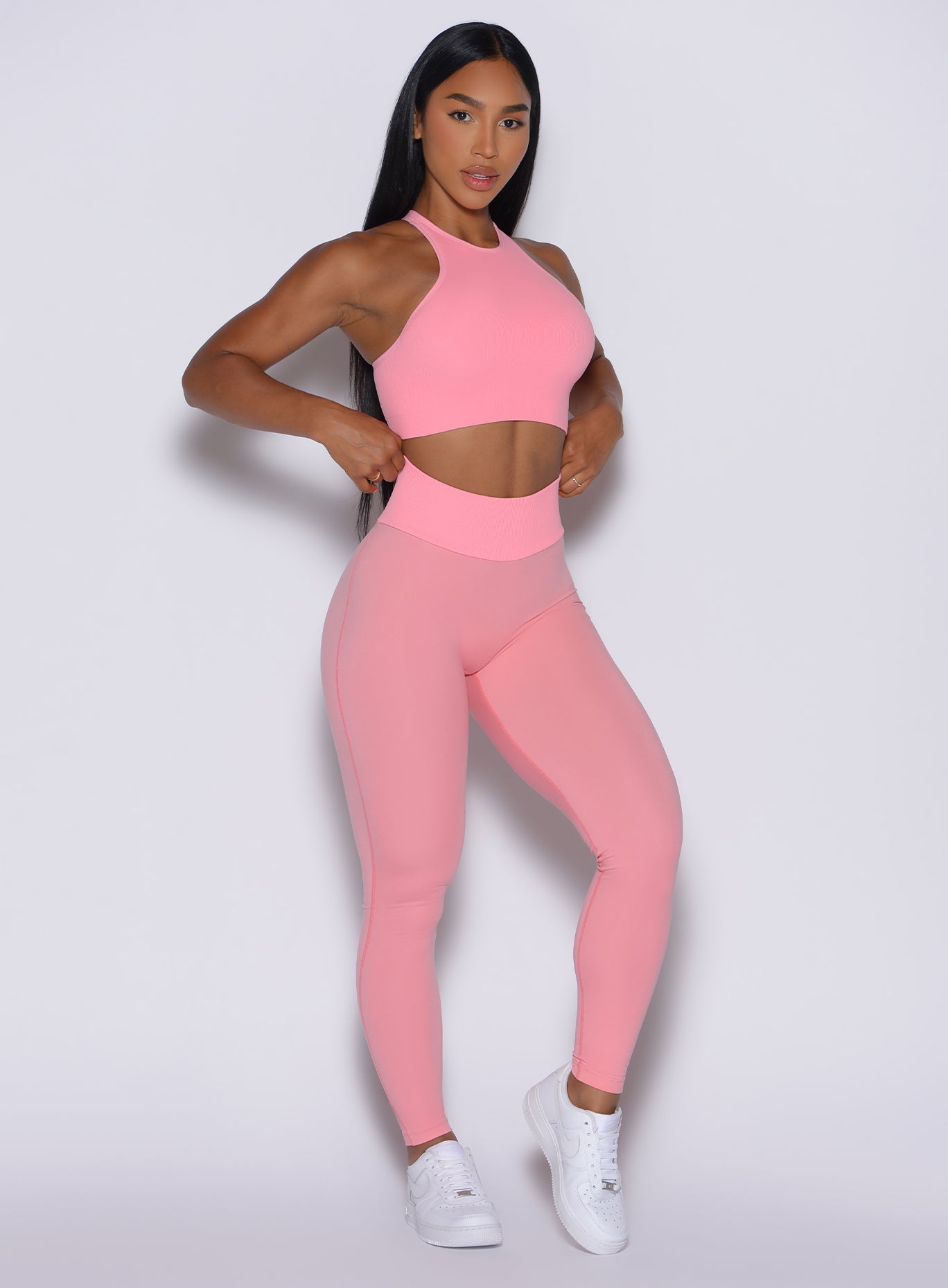 Front right side profile view of our model with both hands on the waist of the leggings wearing the Figure Scrunch Leggings in Peach Burst color