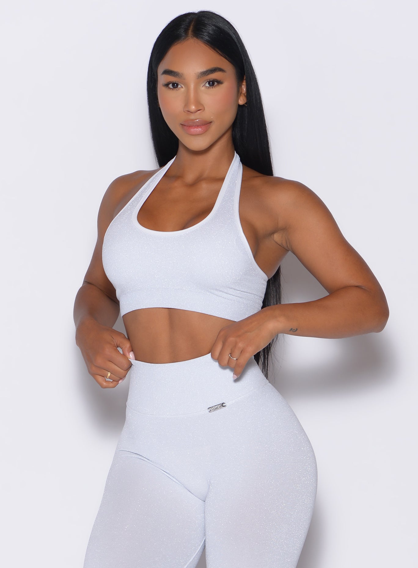 front profile view of a model adjusting the waistband of the leggings wearing the Shimmer Backless Bra in White star color