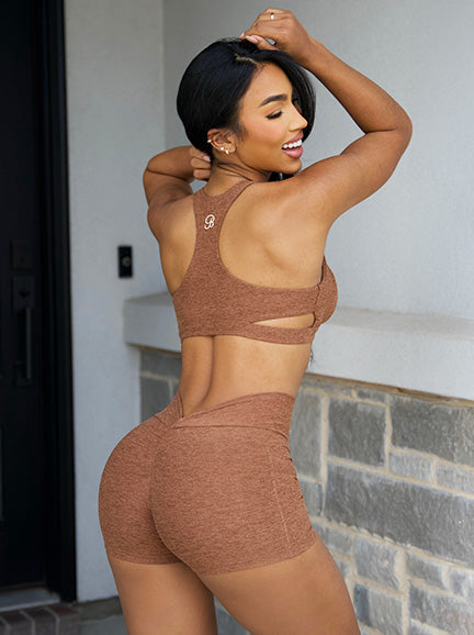 A woman poses outdoors in a brown seamless athletic set, featuring a racerback sports bra with cutout details and matching high-waisted shorts.