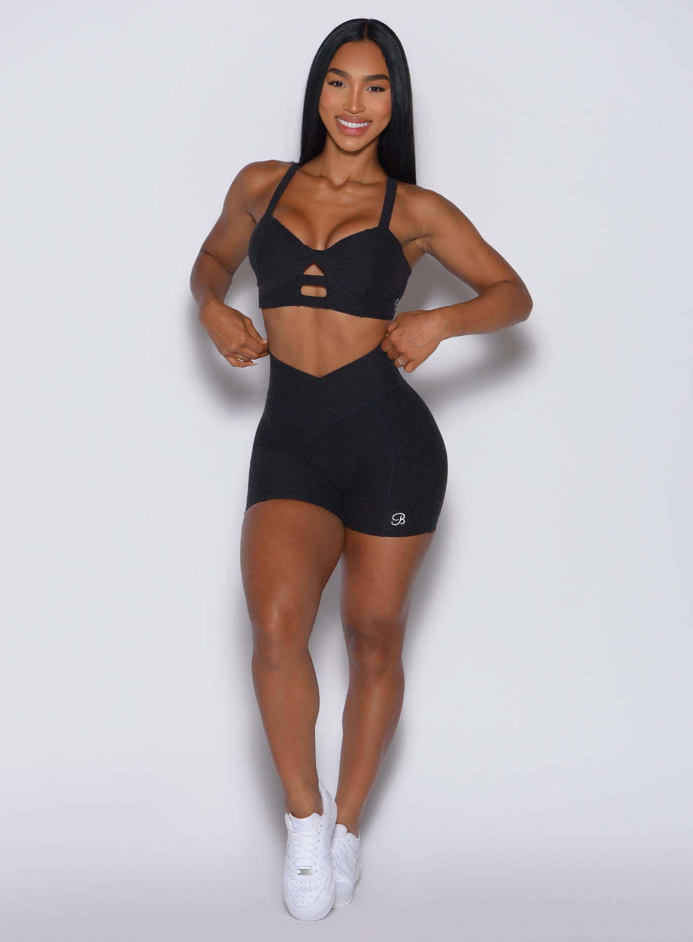 front profile view of a model wearing our Tiny Waist Shorts in Onyx color and a matching sports bra