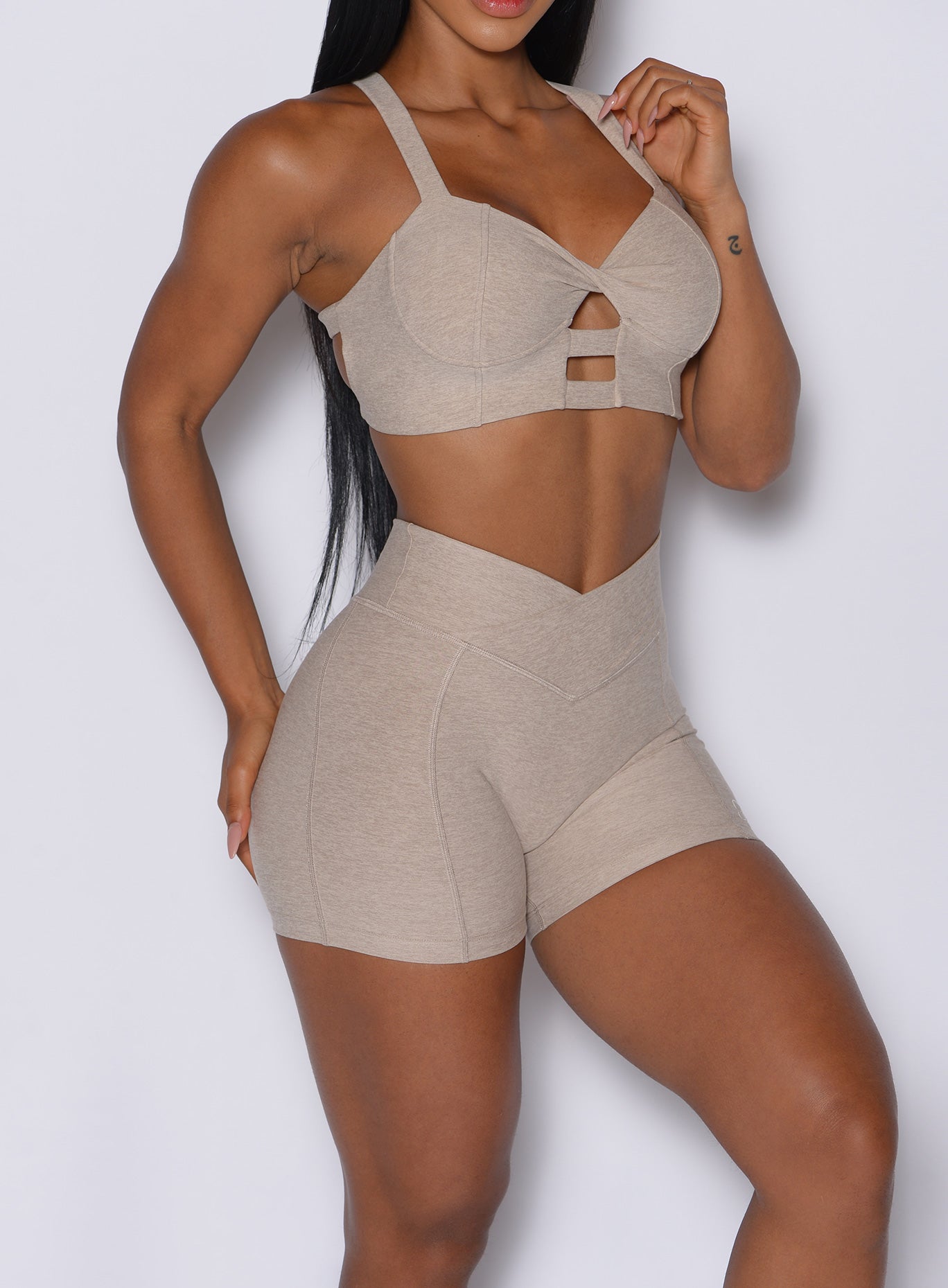 zoomed in right side picture of a model facing slightly to her front wearing our Tiny Waist Shorts in Taupe color and a matching sports bra