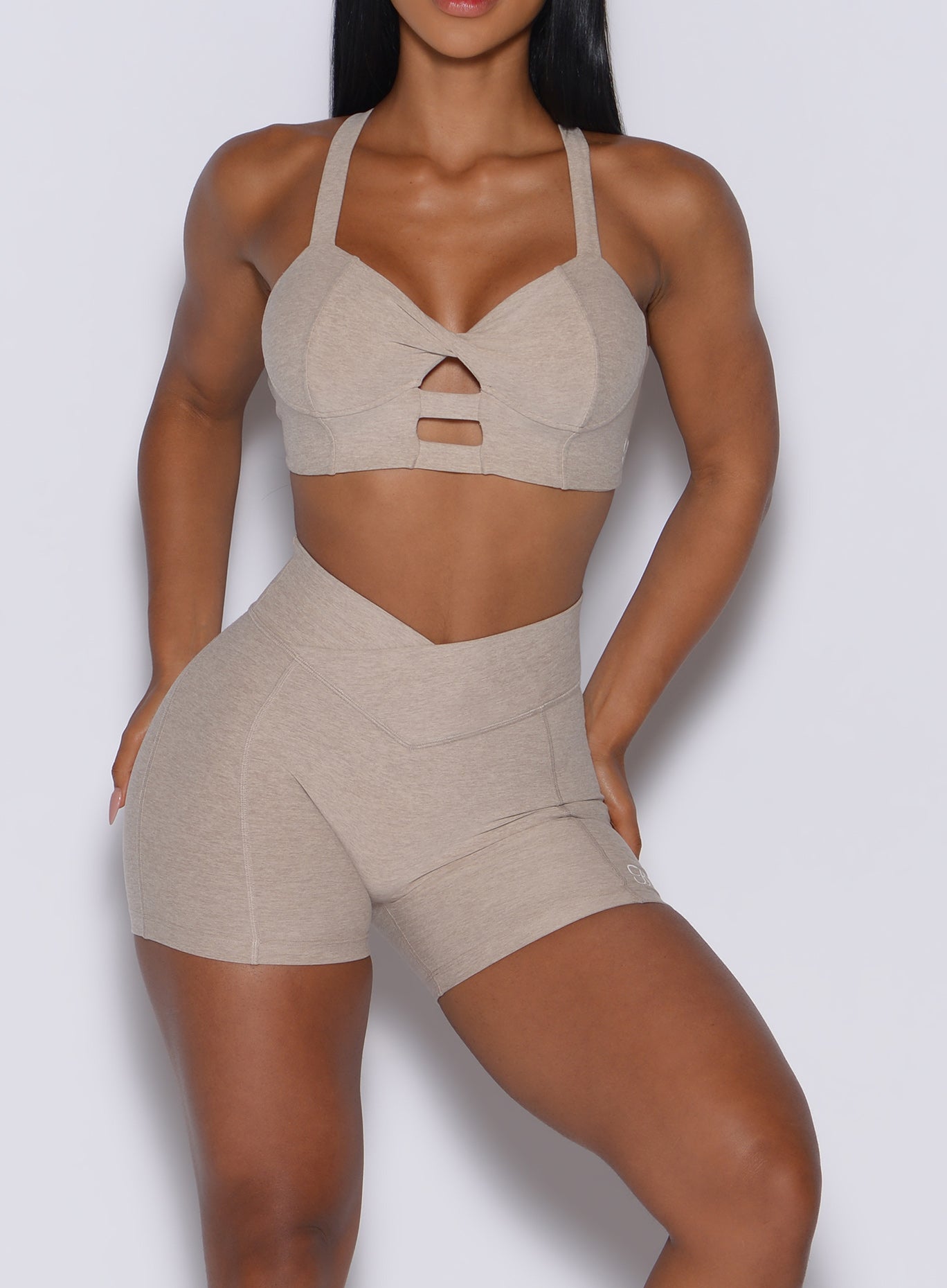 zoomed in front view of a model wearing our Tiny Waist Shorts in Taupe color and a matching sports bra