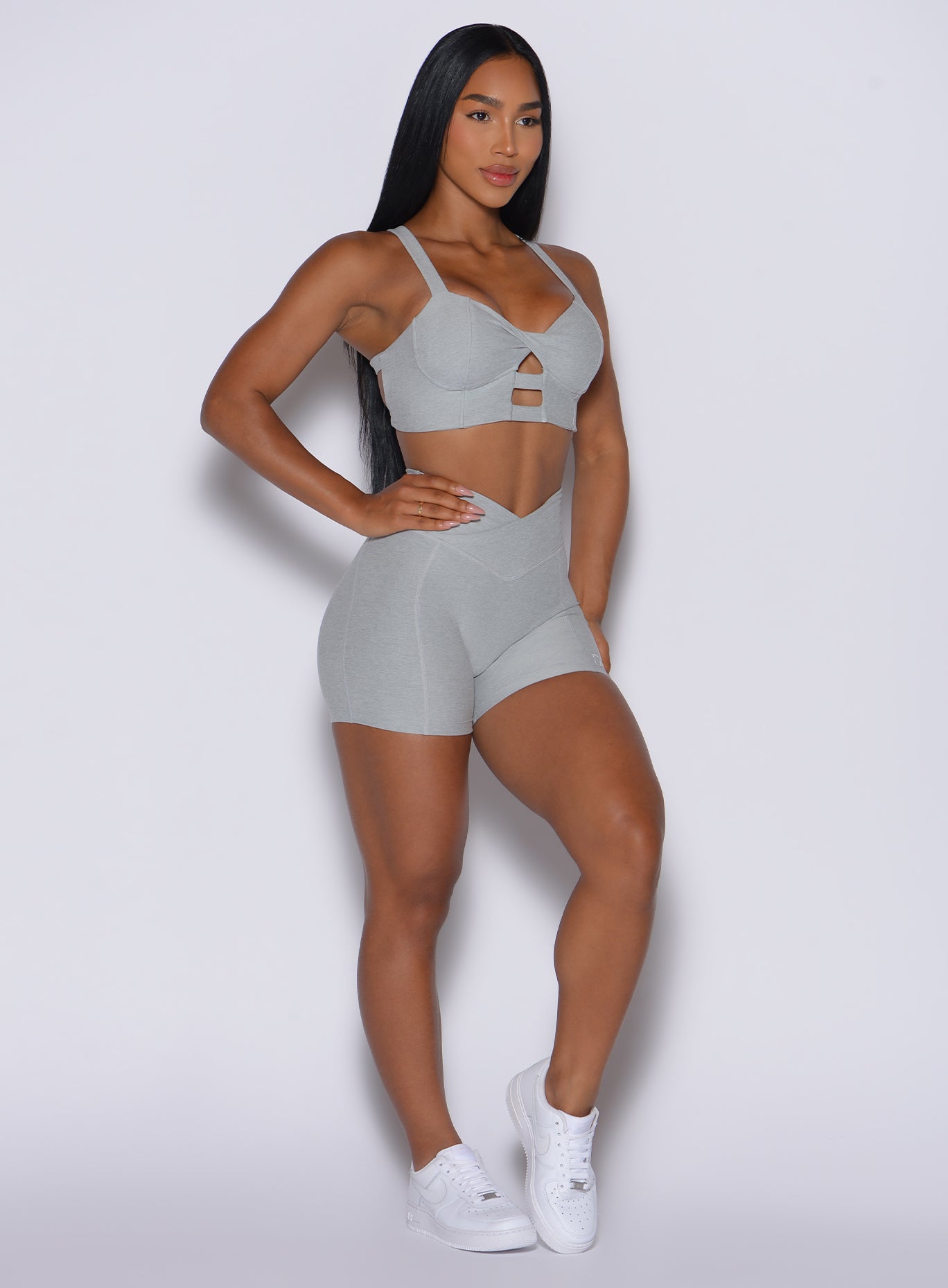 front profile view of a model slightly angled to her left wearing our Tiny Waist Shorts in Light Cloud color and a matching sports bra
