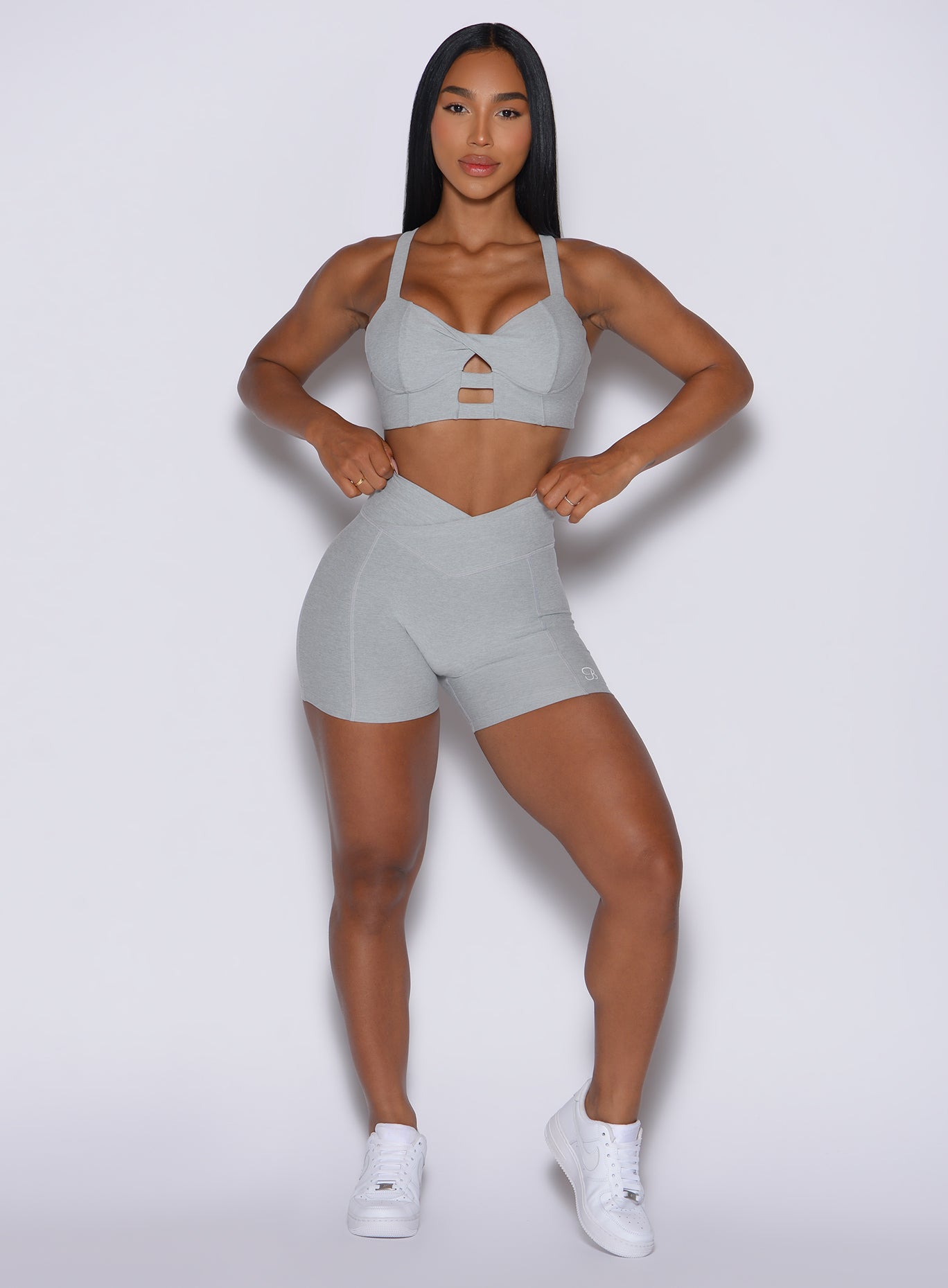 front profile view of a model wearing our Tiny Waist Shorts in Light Cloud color and a matching sports bra