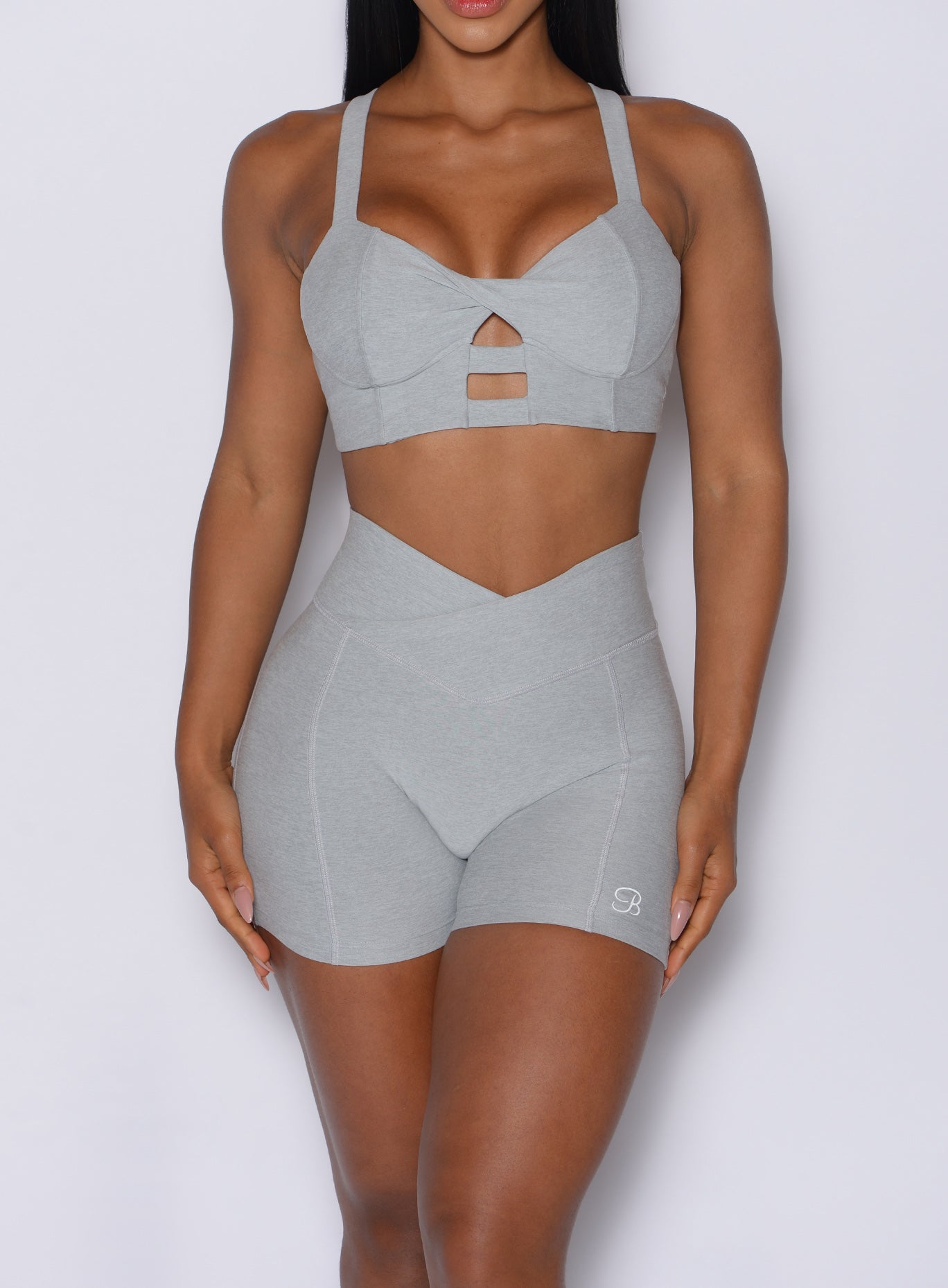 zoomed in front view of a model wearing our Tiny Waist Shorts in Light Cloud color and a matching sports bra