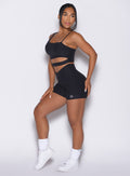 left side view of a model facing to her left wearing our Tiny Waist Shorts and the matching Asymmetrical Slit Bra in Heathered Black color