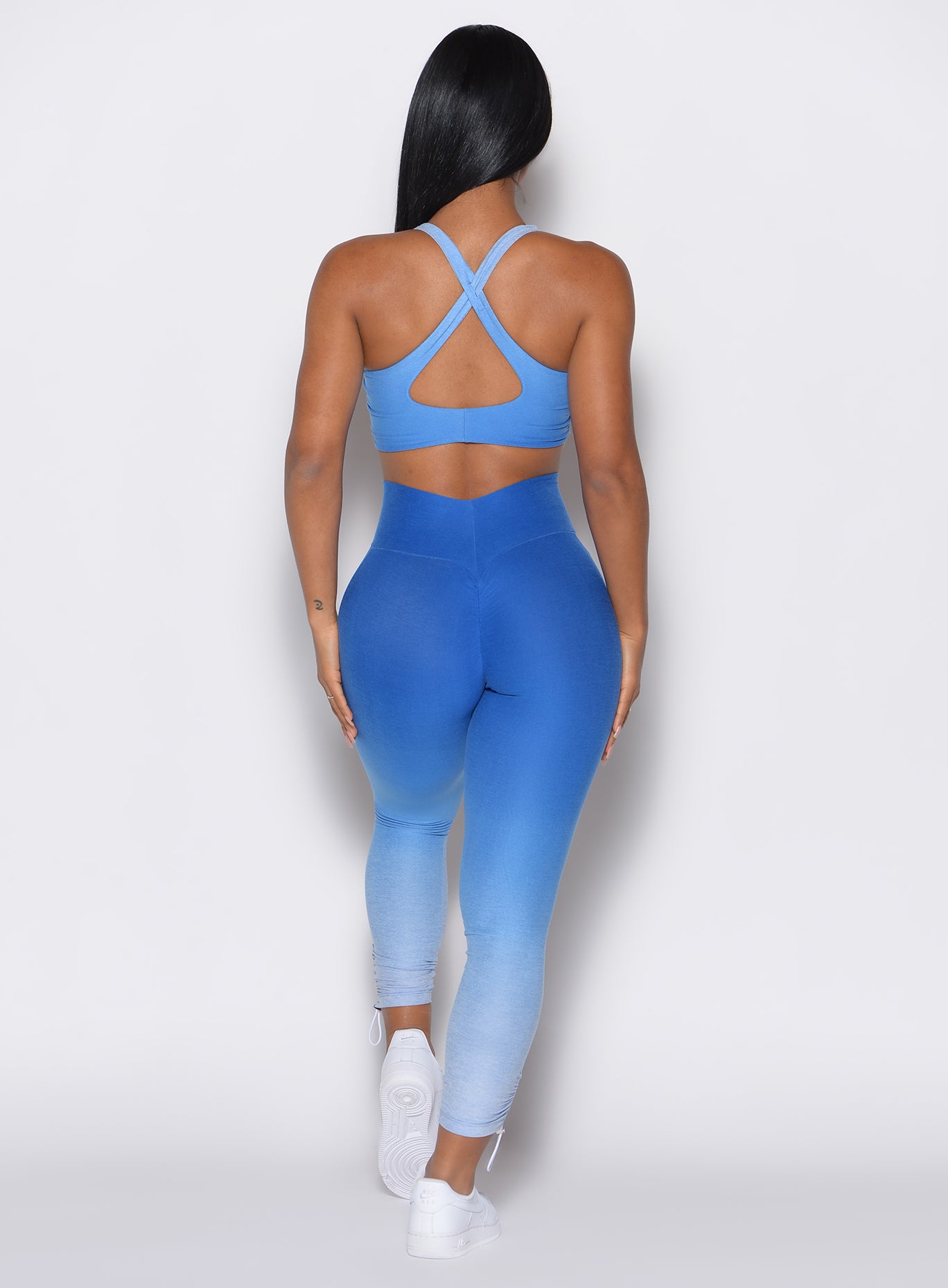 back profile view of a model wearing our toggle leggings in Ombre Blue Crush color along with the matching sports bra