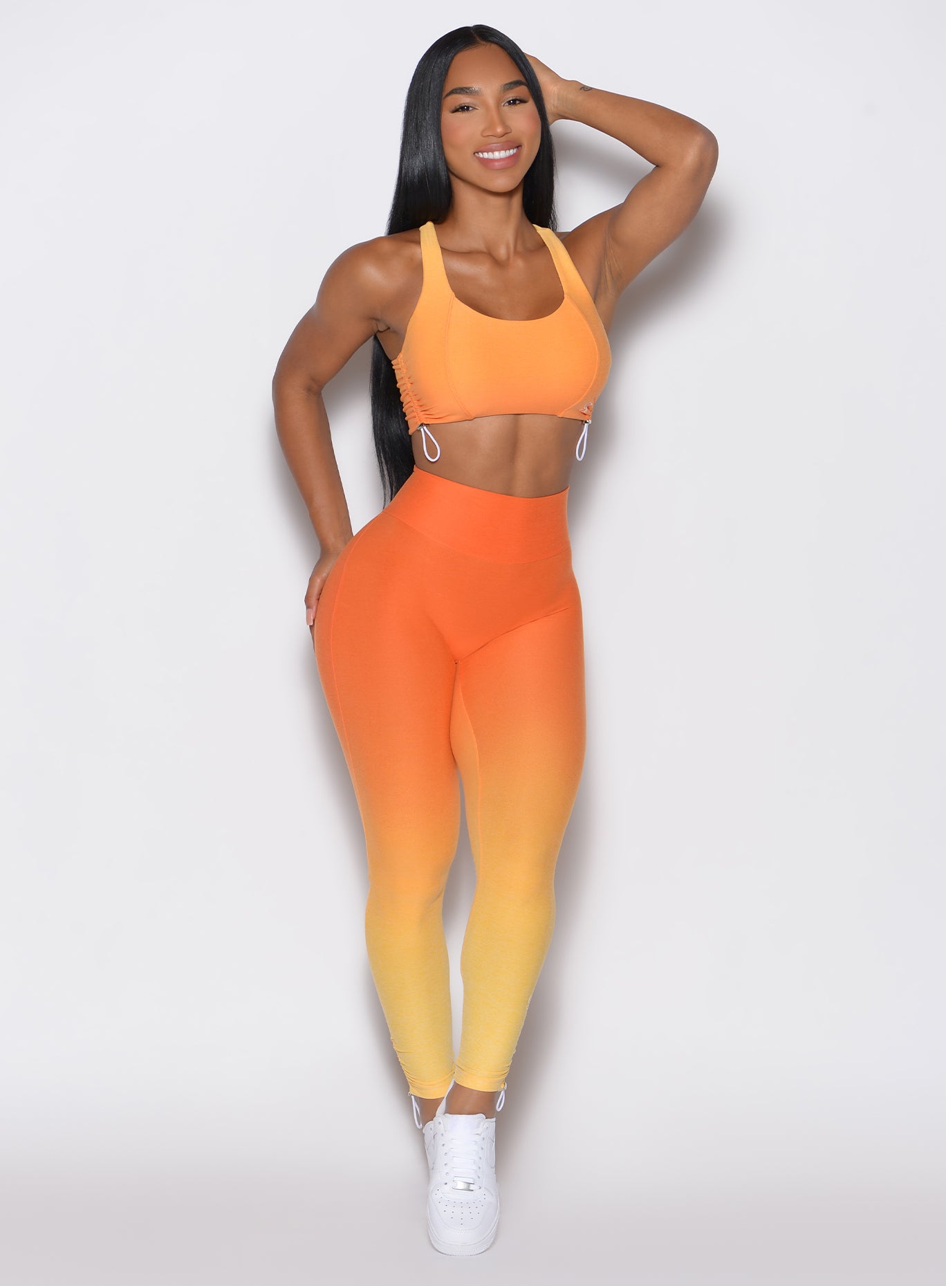 front profile view of a model wearing our toggle leggings in Ombre Hawaiian Punch color along with the matching sports bra 