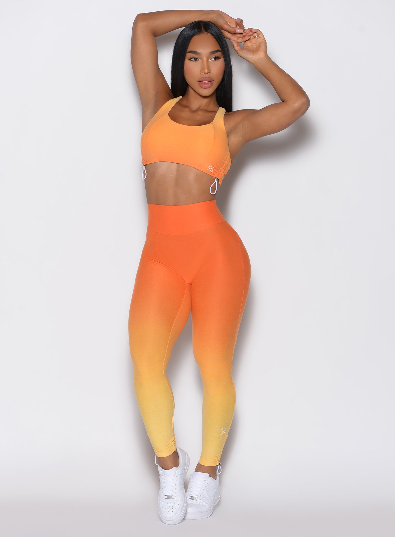 front profile view of a model facing forward with her hands over her head  wearing our toggle leggings in Ombre Hawaiian Punch color along with the matching sports bra