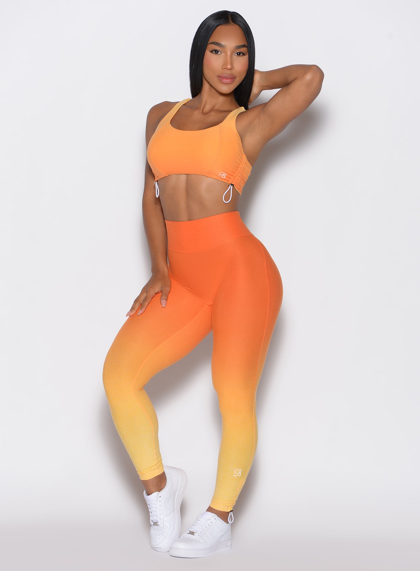 front profile view of a model with her left hand over her neck  wearing our toggle leggings in Ombre Hawaiian Punch color along with the matching sports bra