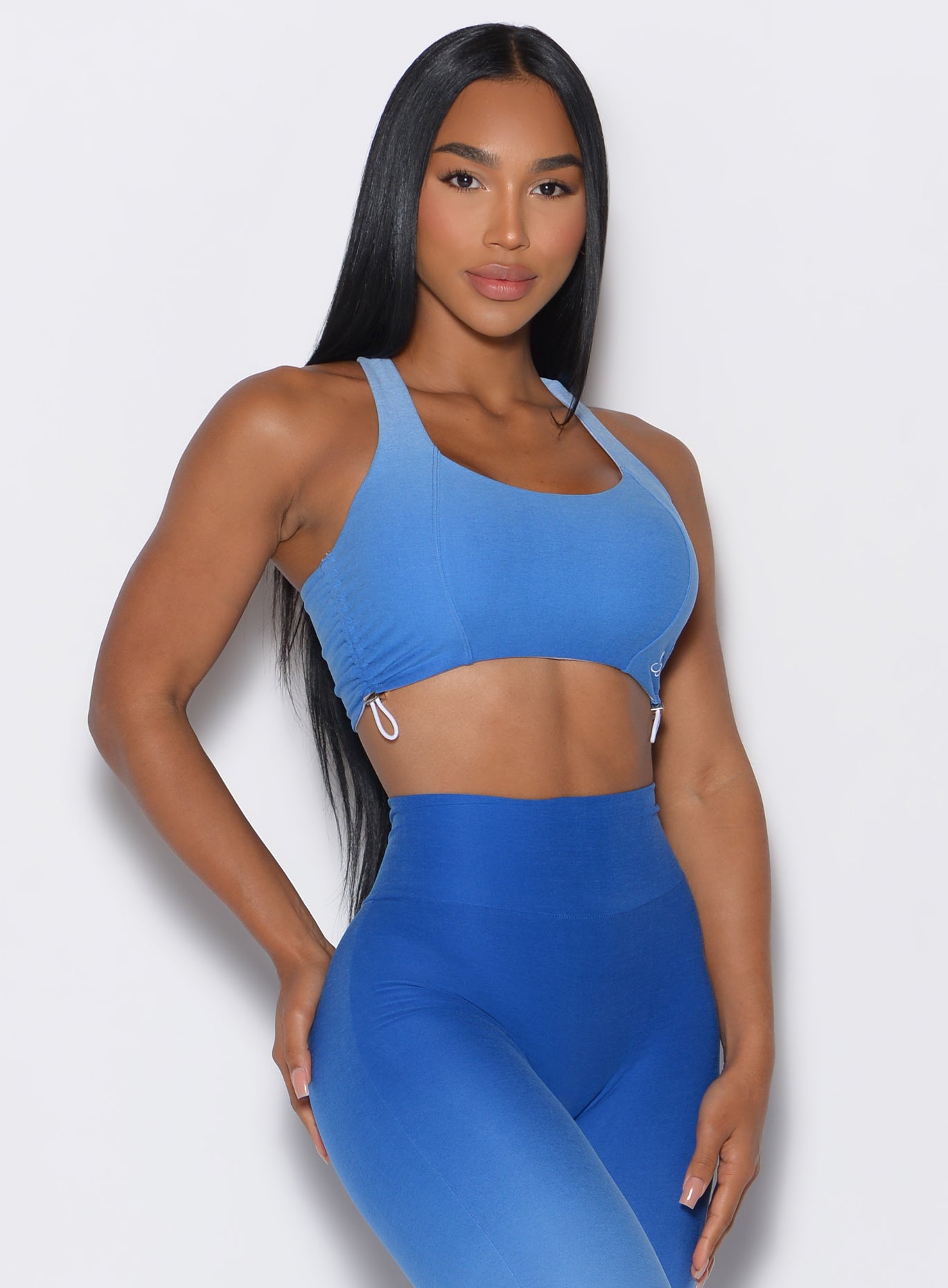 front profile view of a model facing forward wearing our toggle sports bra in Ombre Blue Crush color along with the matching leggings