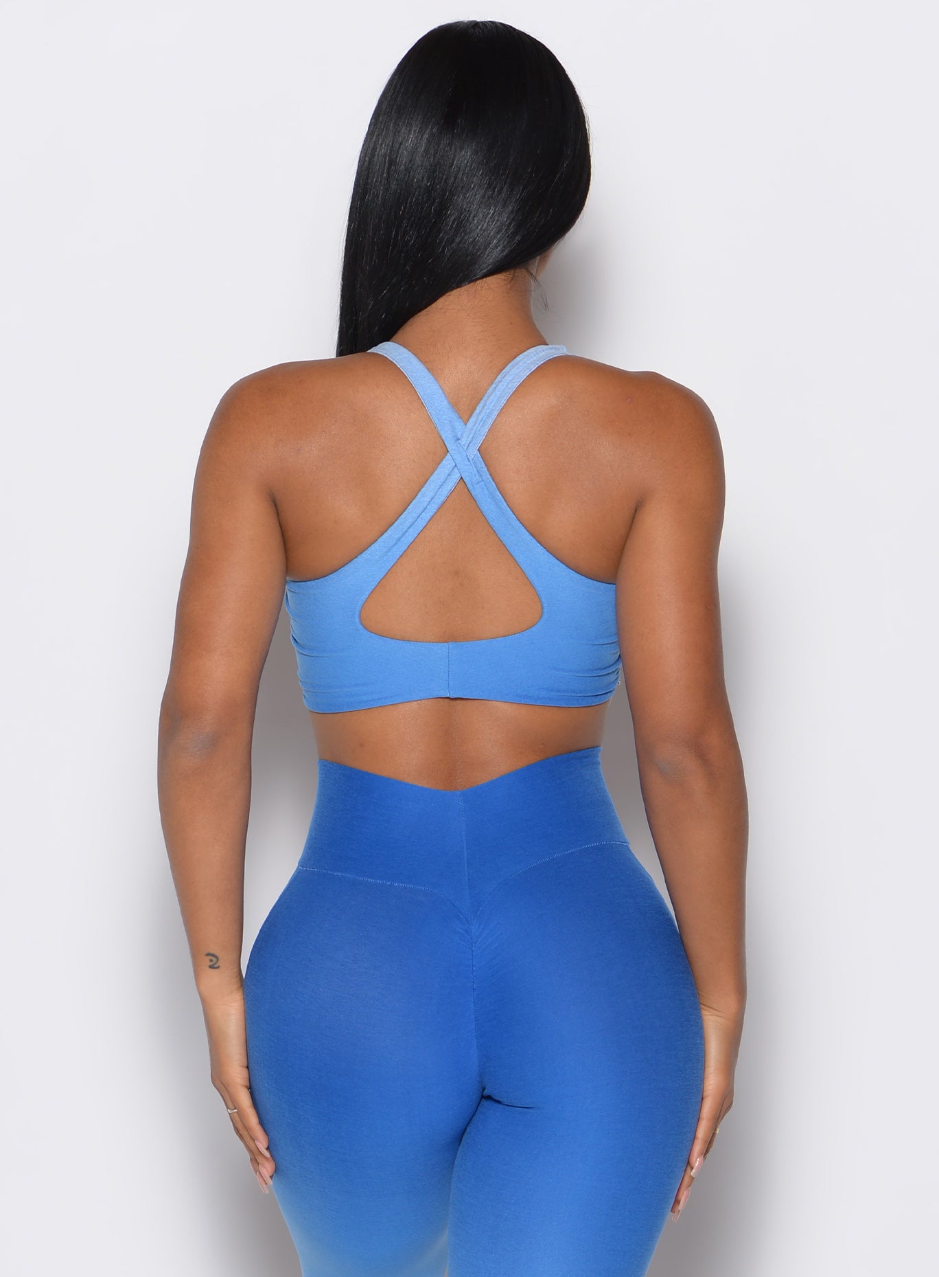 back profile view of a model wearing our toggle sports bra in Ombre Blue Crush color along with the matching leggings
