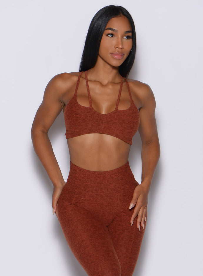 Front profile view of a model wearing our topnotch sports bra in cinnamon color along with a high waist leggings 