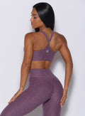 Back profile view of a model wearing our top notch bra in regal purple color along with the matching leggings