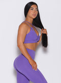 Right side profile view of a model wearing our twist sports bra in royal purple color along with the matching leggings