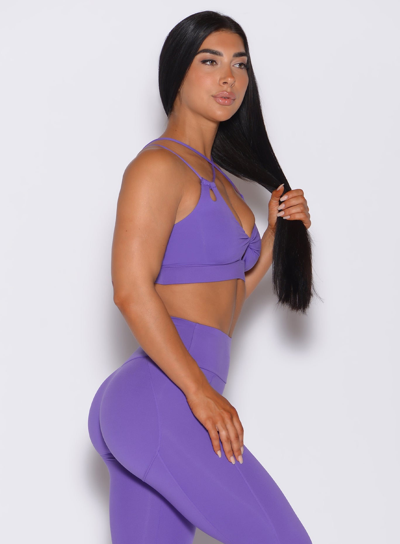 Right side profile view of a model wearing our twist sports bra in royal purple color along with the matching leggings